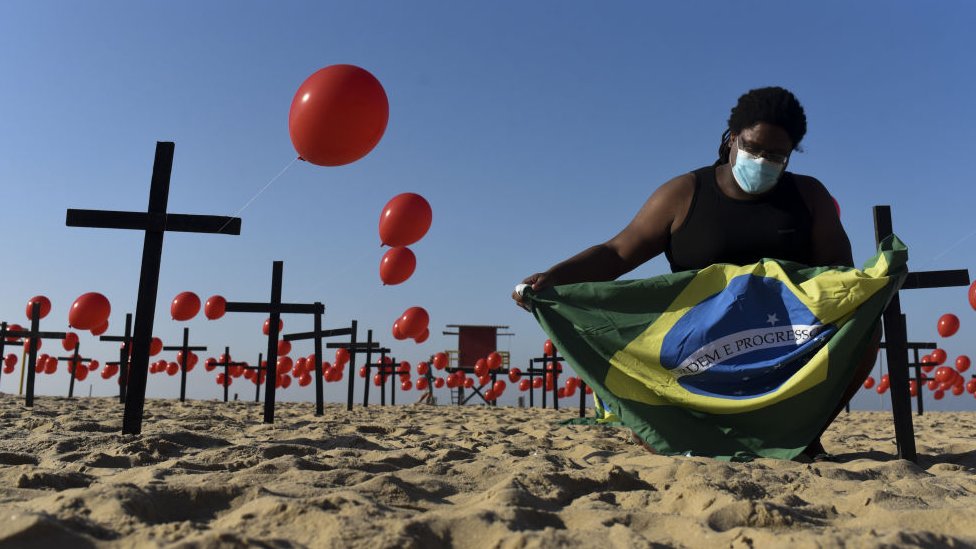 Homem segura bandeira do Brasil em meio a balões vermelhos, representando vítimas de covid-19, no Rio de Janeiro