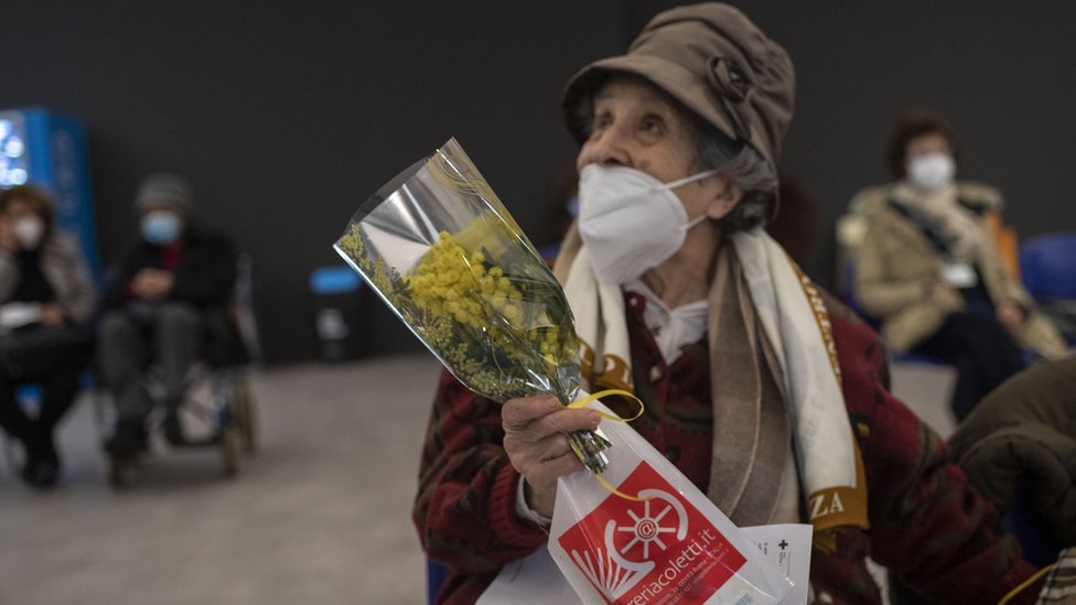 A woman receives mimosa flowers at a vaccination hub in Rome, Italy on International Women's Day 2021.