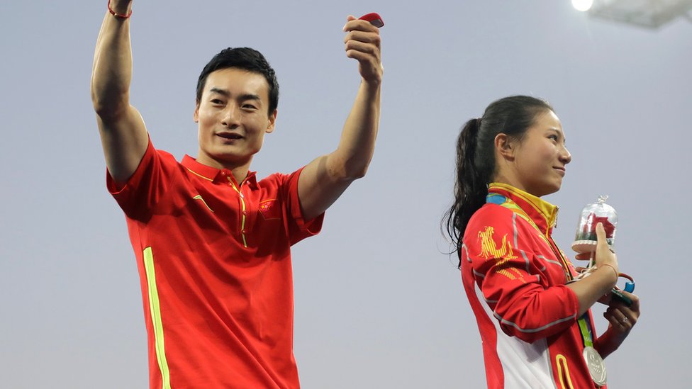 Цинь Кай показывает палец вверх после того, как серебряный призер Хэ Цзы принял его предложение