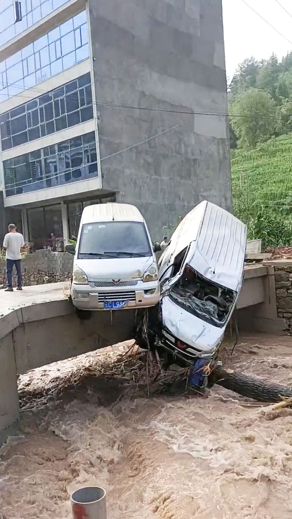 ​​Vehicles hang over the edge of a bridge above flood waters following heavy rainfall in Zhenxiong County, Yunnan Province, China - 2 July 2023