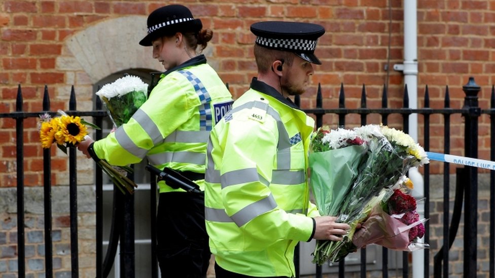 Полицейские несут цветы, оставленные на месте множественных ранений в Рединге