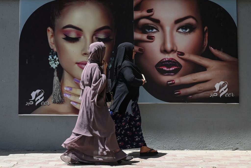 Mujeres con burka caminan frente a retratos de otras mujeres maquilladas en Kabul, el 7 de agosto de 2021.