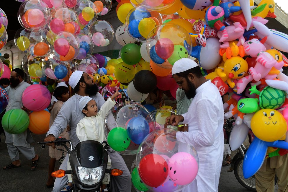 Dete pokazuje prstom na balon dok sedi na motociklu pored roditelja