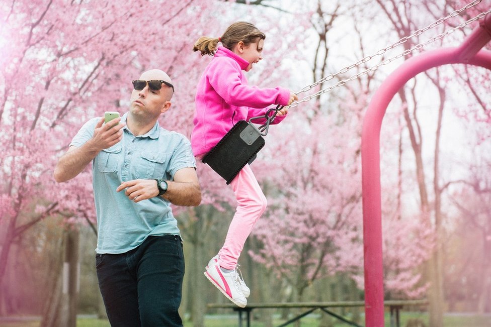 Un padre mirando el teléfono mientras su hija está en un columpio