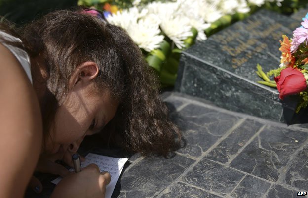 Girl writing note at grave of Pablo Escobar
