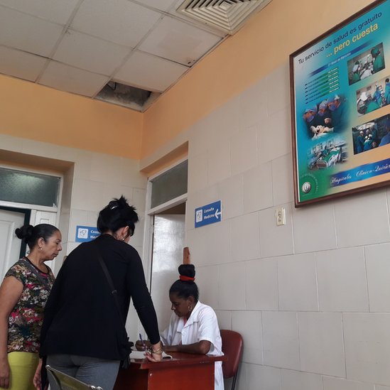 Una de las salas de espera con los carteles del costo de la salud y los pacientes esperando en el Hospital General Calixto García. Consulta médica en Cuba