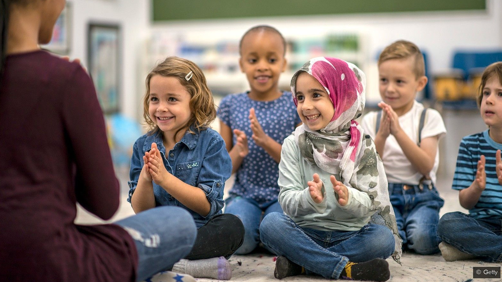 Children in a classroom, sitting on the carpet clapping hands