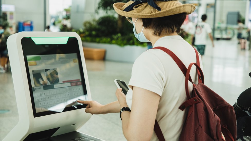 Una mujer realiza una facturación en una máquina de un aeropuerto.