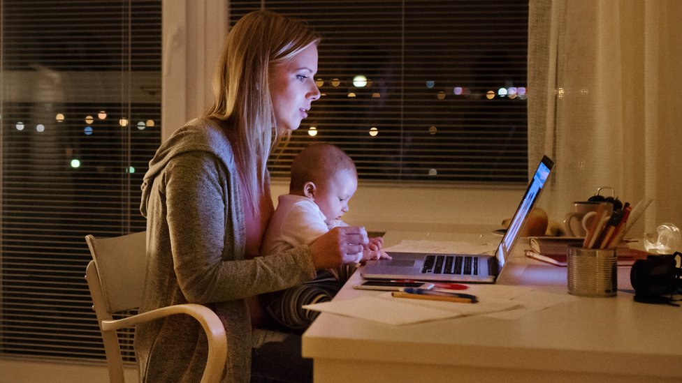 Мать с сыном на руках работает на ноутбуке