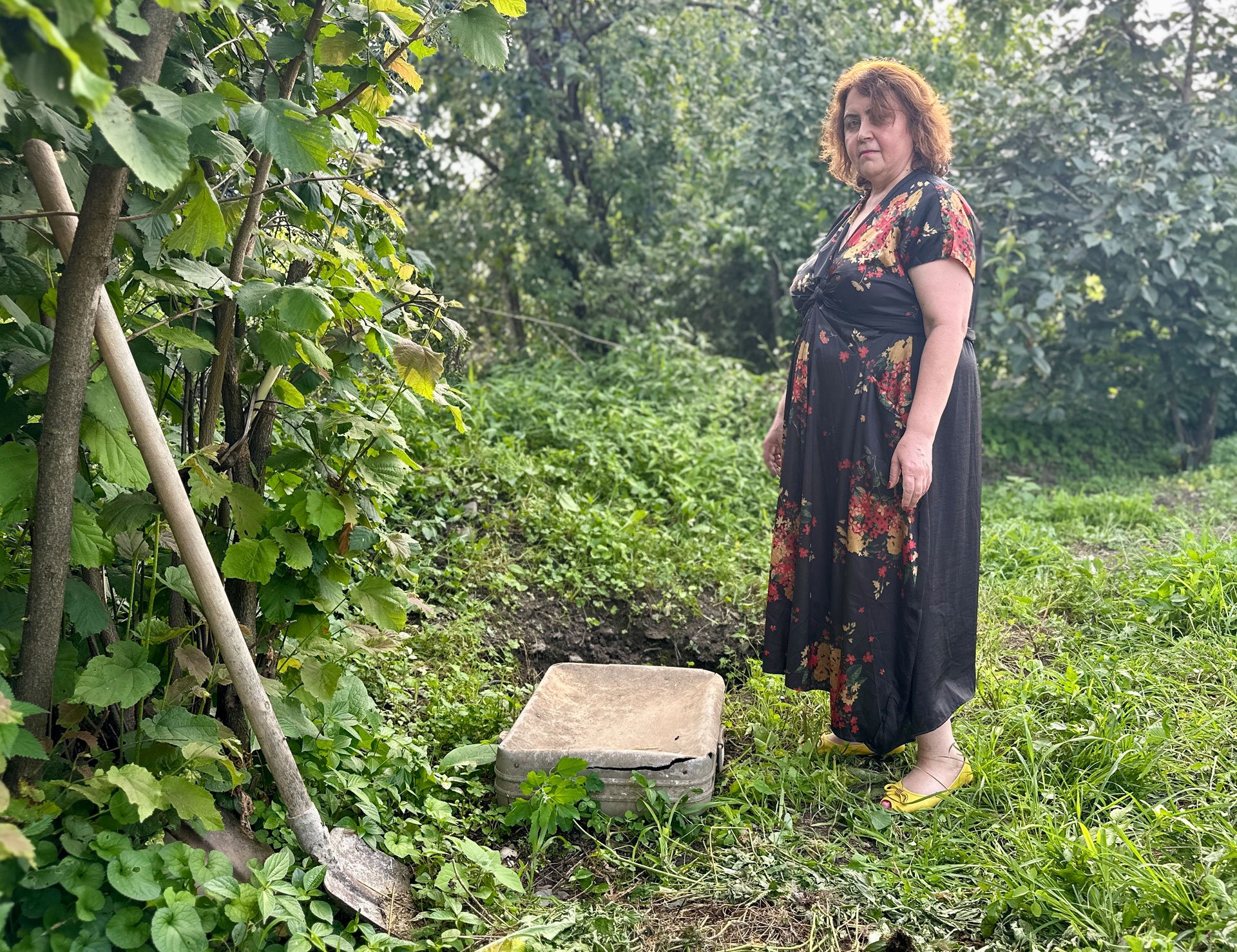 Irina's daughter Nino Elizbarashvili stands next to a suitcase and a shovel in the garden