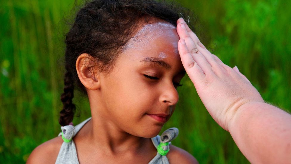 Mãe passa protetor solar no rosto da filha antes do evento Annual Pony Swim na ilha de Chincoteague, EUA