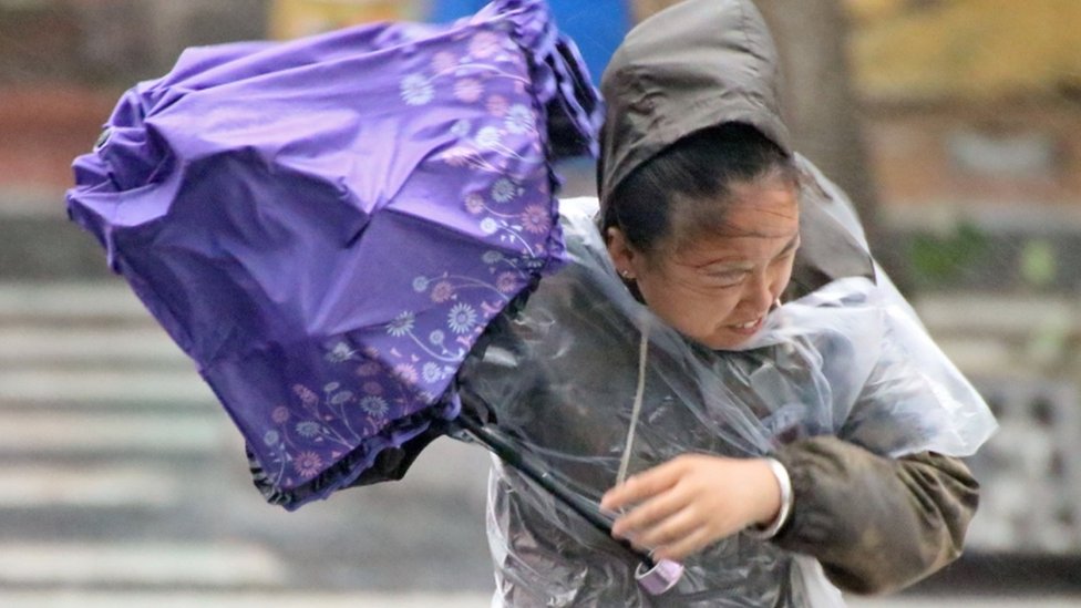 Женщина держит зонтик от ветра и дождя, принесенных тайфуном Лекима в Яньтай, Шаньдун