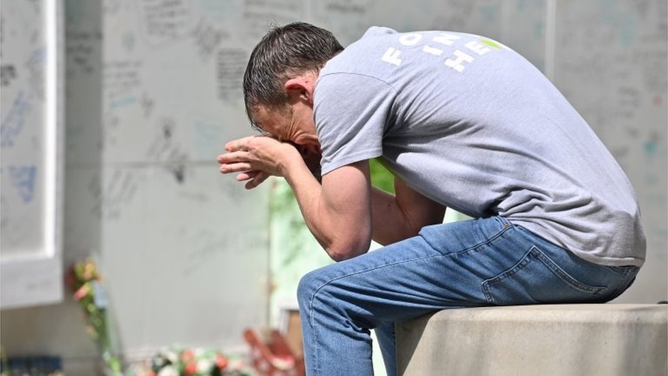 Мужчина плачет, сидя на стене возле мемориальной стены Гренфелла