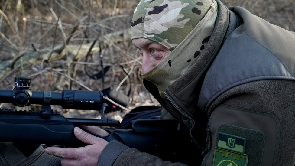 Aleks na glavi nosi vojničku masku i vežba gađanje snajperkom puškom
