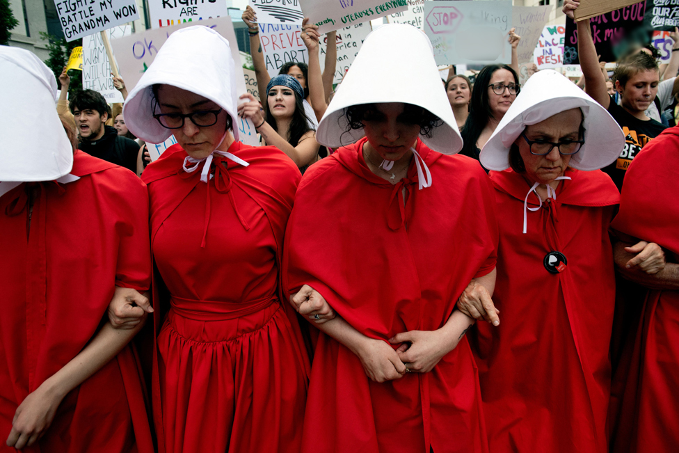 ناشطات في الحملة من أجل الحق في الإجهاض يتظاهرن في مدينة دنفر في كولورادو في زي مستقى من المسلسل التلفزيوني The Handmaid's Tale بعد أن ألغت المحكمة الدستورية الأمريكية الحق الدستوري في الإجهاض.