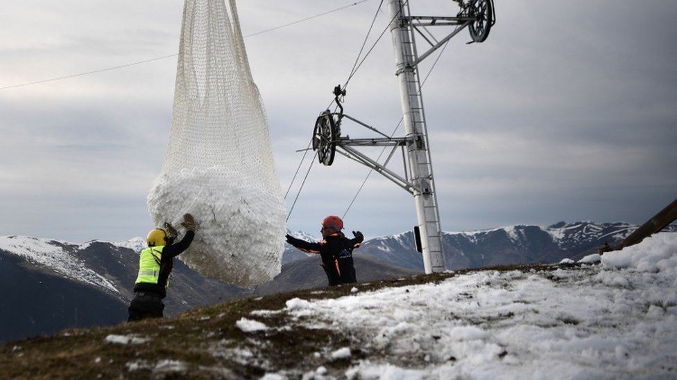 Двое мужчин помогают вертолету, перевозящему снег возле Люшона во французских Пиренеях