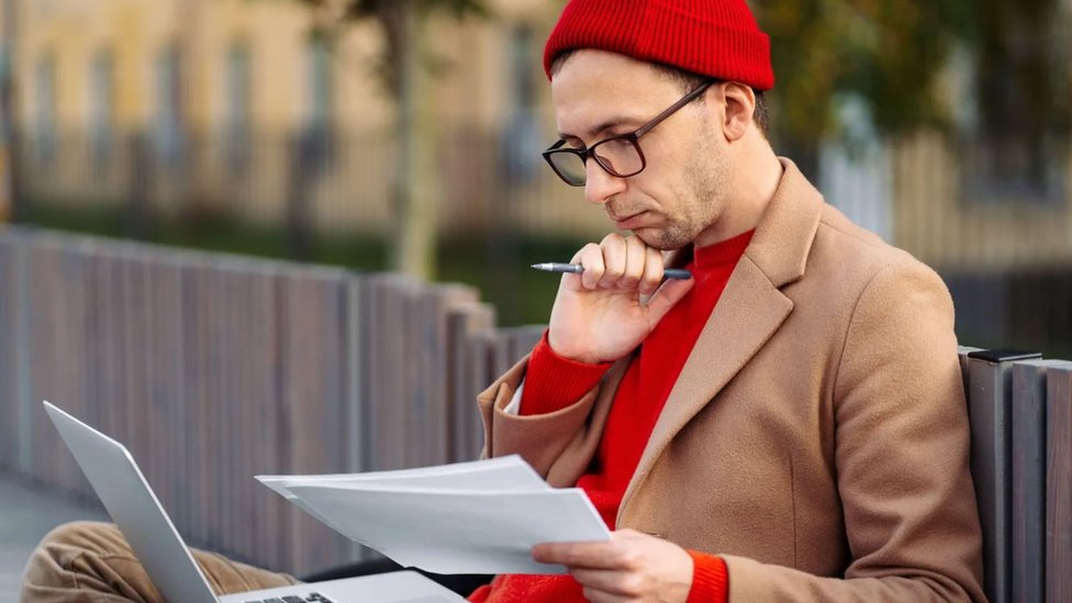 Un hombre con una computadora y un bolígrafo en la mano pensando.