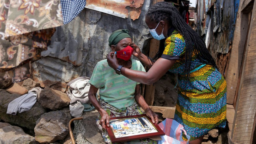 Видно, как член местной организации жертвует маску пожилой женщине в трущобах Матаре на фоне пандемии коронавируса.