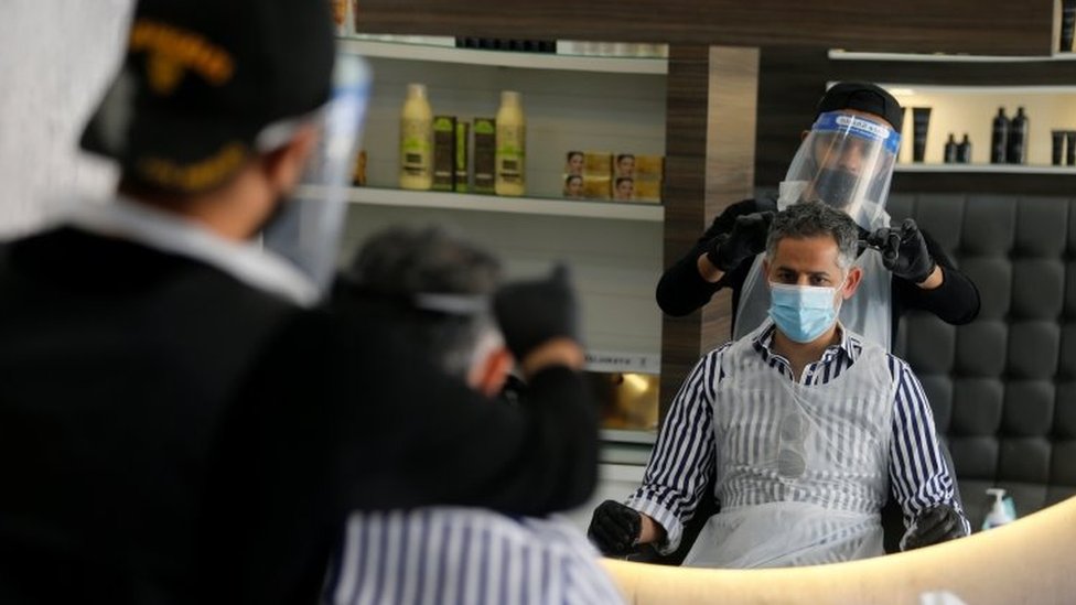 Парикмахер в защитном снаряжении подстриг мужчине волосы в Иса-Тауне, Бахрейн (27 мая 2020 г.)