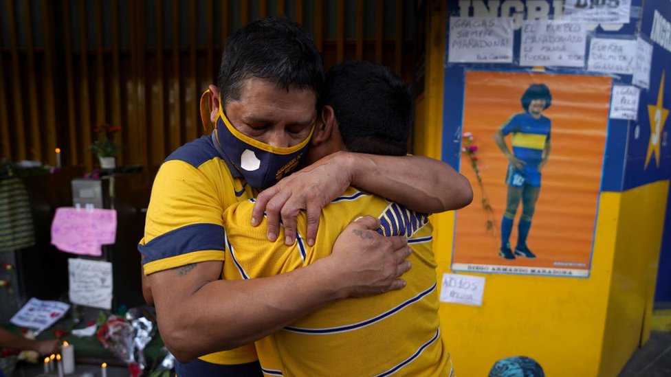 Seguidores se abrazan por la muerte de Diego Maradona.