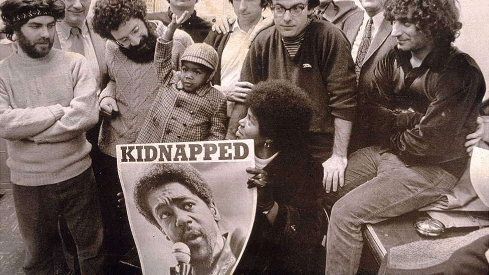 Реальная Чикаго Семерка держит плакат с изображением Бобби Сила, обвиненного в убийстве, похищении и заговоре
