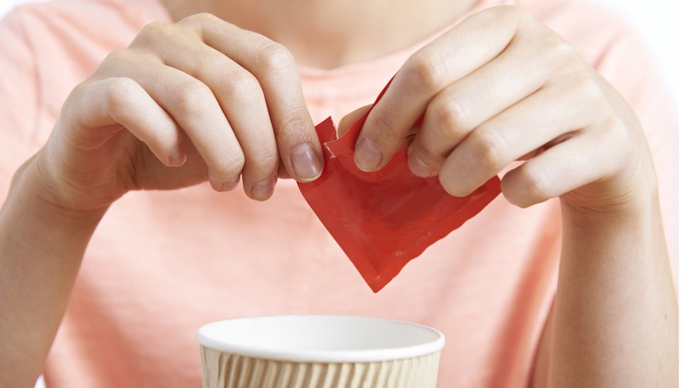 Mujer añadiendo edulcortante al café.