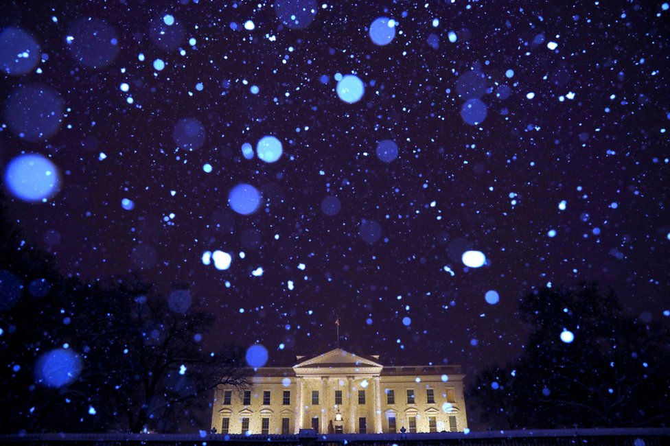 Snow is seen falling at night in front of the White House