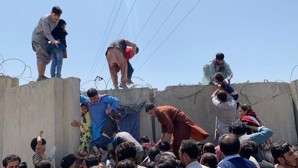 Personas escalando el muro que encierra el Aeropuerto Internacional Hamid Karzai