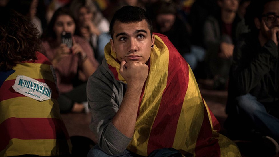Un joven escucha la comparecencia de Mariano Rajoy en una pantalla de televisión de Barcelona el día del intento de referéndum en Cataluña. Joven en Barcelona.