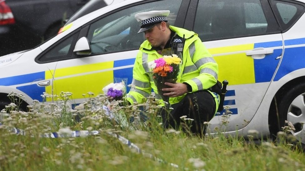 Полицейский возлагает цветы на месте убийства констебля Эндрю Харпера