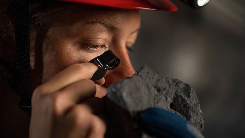 Una mujer observa de cerca una roca en una mina