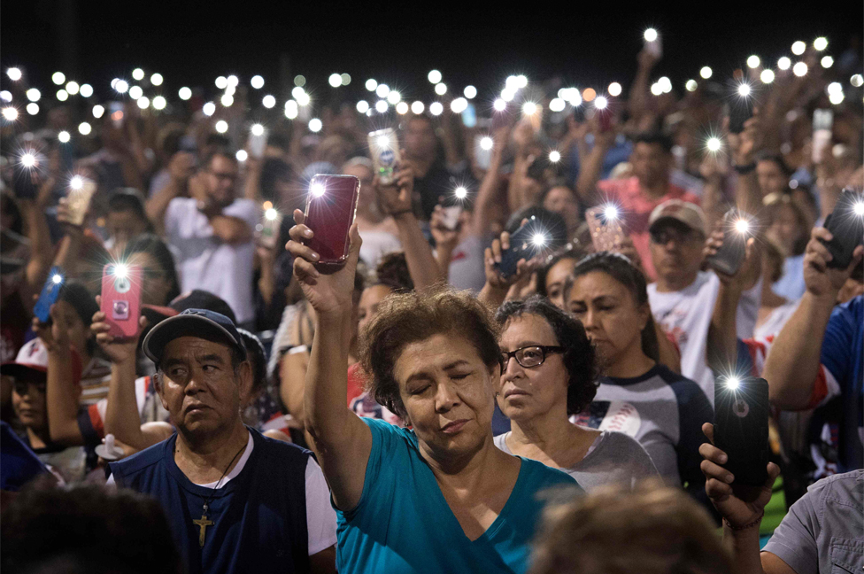People hold up their phones during a prayer vigil