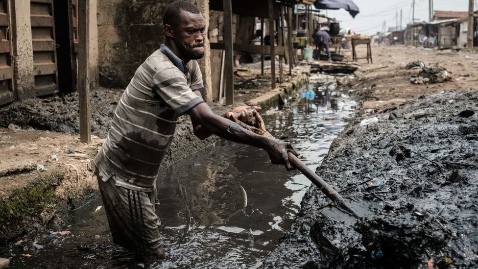 Мужчина убирает ил из канавы для улучшения дренажной системы в районе Мосафеджо в Лагосе 12 февраля 2019 г.