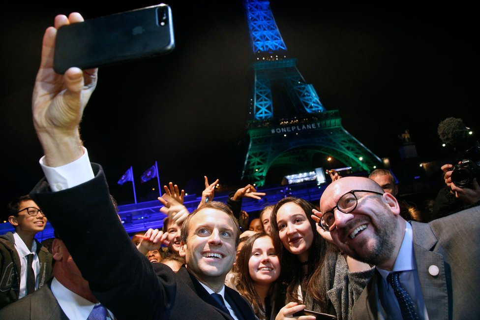 Президент Франции Эммануэль Макрон использует свой iPhone, чтобы сделать селфи с толпой перед Эйфелевой башней