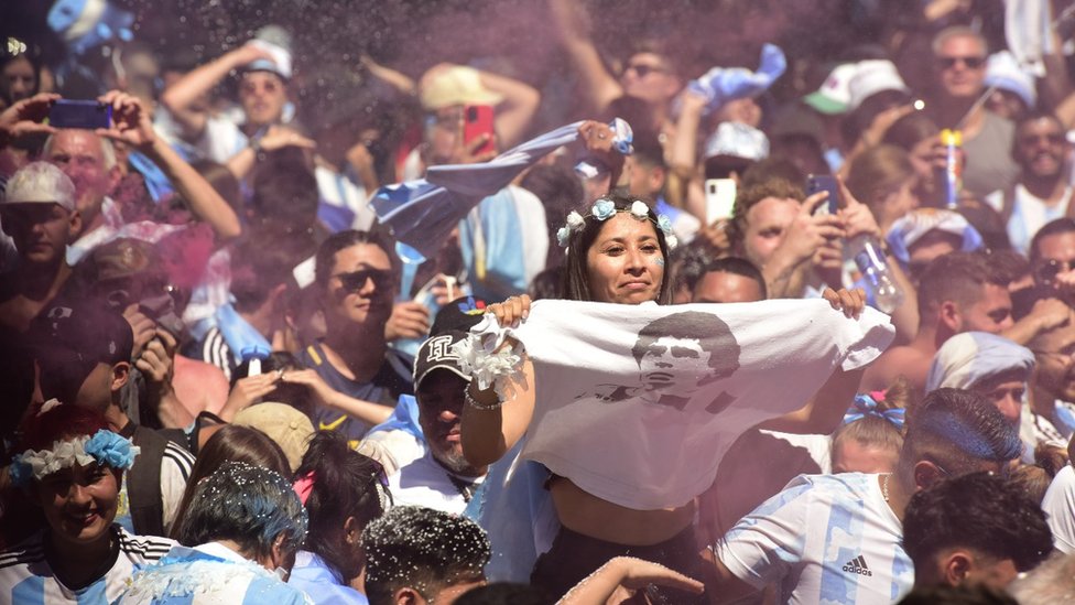 Una mujer sostiene una tele con la cara de Maradona.