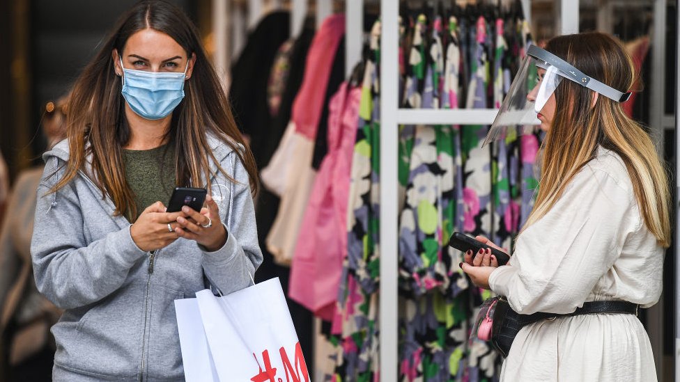 A woman wearing a mask walks out of a clothes shop