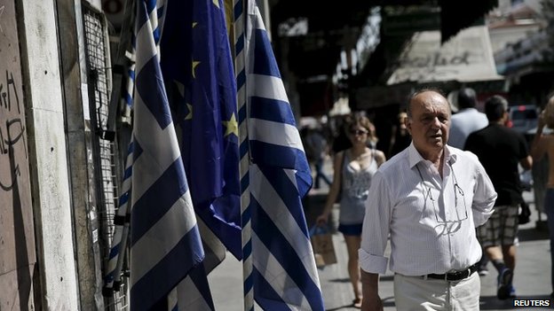 Мужчина идет рядом с национальными флагами Греции и флагом Европейского Союза в центре Афин
