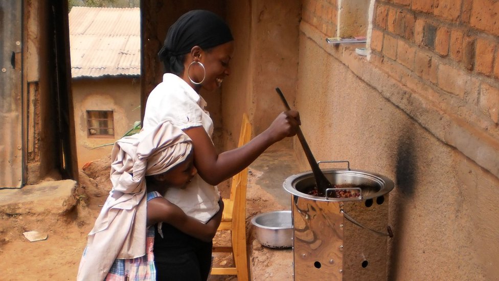Женщина в Руанде с ребенком готовят еду на топливной плите