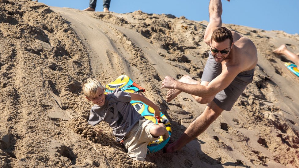 Uncle and nephew sled down a sand dune in Hermosa Beach, California, on 26 November 2020