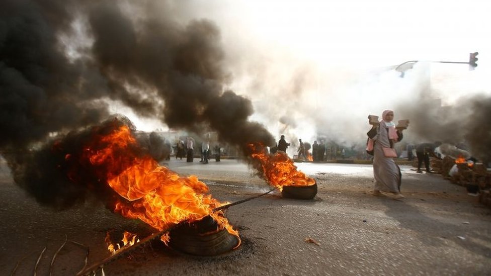 متظاهرة سودانية تمر بجوار إطار مشتعل بالقرب من مقر وزارة الدفاع في الخرطوم