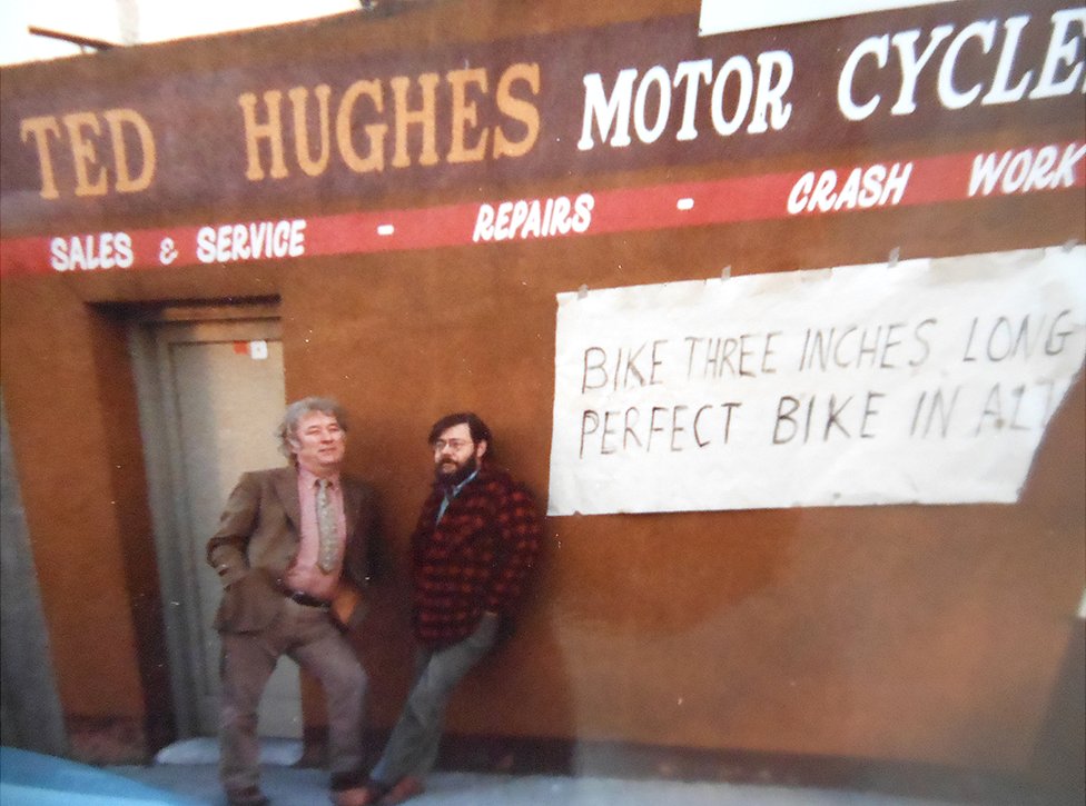 Симус Хини и Барри Кук позируют под вывеской мотоциклов Теда Хьюза в Дублине (1985 г.), сразу после того, как Тед Хьюз был назначен лауреатом поэтессы