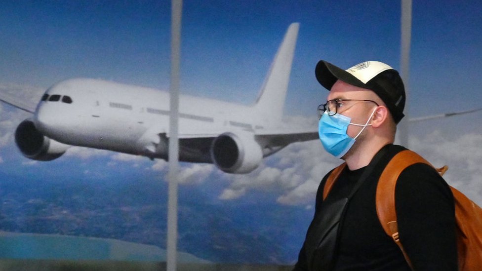 Hombre con mascarilla con un avión detrás.