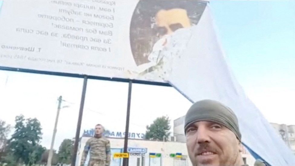 Ukrainian servicemen pull a Russian poster off a billboard, revealing a poem by Taras Shevchenko, Sept 2022