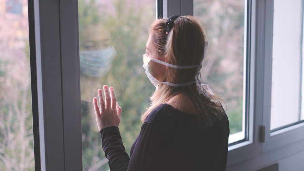Mujer con mascarilla mirando por una ventana