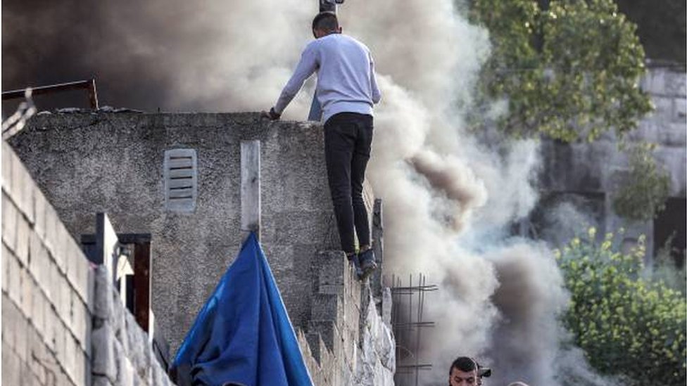 فلسطيني يعتلي سطح بناية وسط أعمدة الدخان خلال مداهمة الجيش الإسرائيلي لمخيم جنين