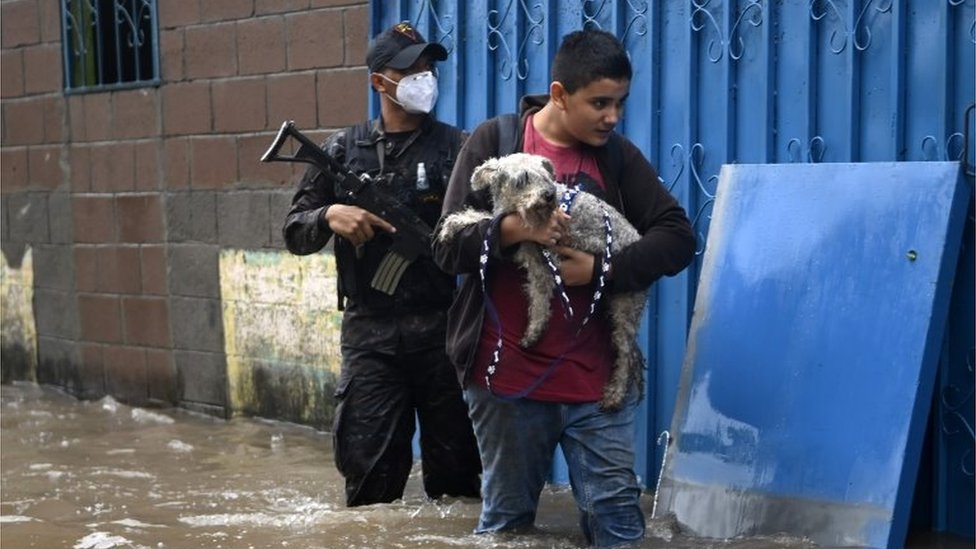 Мальчик несет свою собаку, когда он пробирается по воде в затопленной колонии Санта-Люсия в Илопанго, Сальвадор, во время тропического шторма Аманда, 31 мая 2020 г.