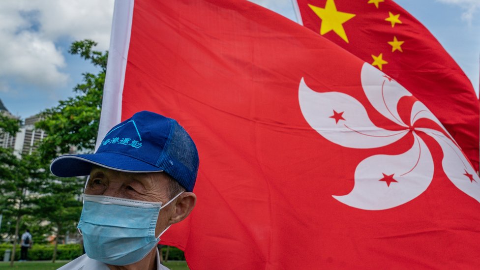 香港親北京陣營慶祝北京頒布《香港國安法》活動上一位戴上口罩的老翁站在中國國旗與香港區旗前（30/6/2020）