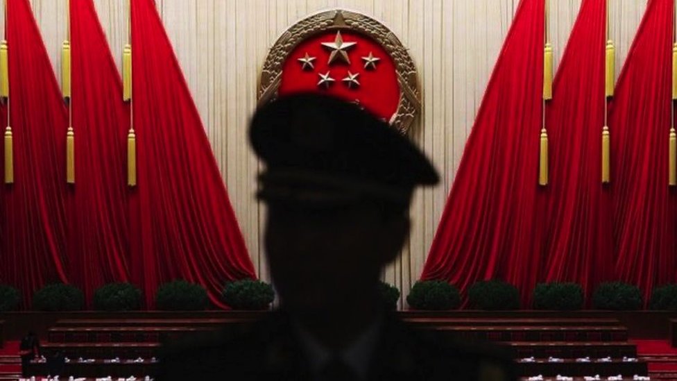 La silueta de un hombre uniformado frente a grandes banderas rojas en un salón