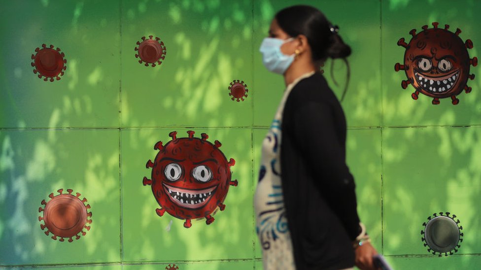 Woman wearing a facemask as a preventive measure against the Covid-19 coronavirus walks past a mural in New Delhi,