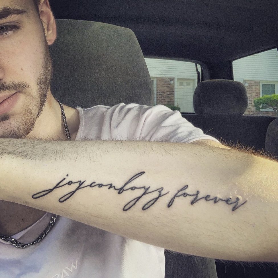 Мужчина демонстрирует свою татуировку. Оно читается как «joyconboyz forever» курсивом.